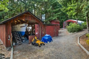 From edge of circular driveway, view of boat/RV storage and wood shop, pump house with 3000 gallon water storage tank, and quonset style shop in the background.