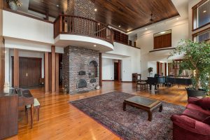 In winter, the masonry brick "Russian Fireplace" may be the center focus when in use. A baking slot above the firebox can cook potatoes, casseroles, even pizza. The cast iron cooktop has a separate smaller firebox, which the owners mostly used during occasional power outages. The balcony above the fireplace provides a calming spot to sit and take in the extraordinary view of the water. The hallway with floor to ceiling book shelves leading to the upper bedrooms and offices is visible at the very top of the image.