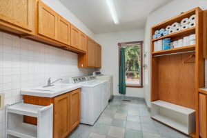 Laundry room, with easy-care tiled floor, has a deep sink and hookups for two sets of washers and dryers, if desired. Overhead cabinets for storage and (not visible in this image), a tiled counter with pull-out laundry baskets and more overhead cabinets for storage.