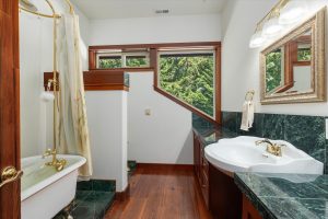 The large upstairs bathroom features a claw foot tub, pedestal sink, green marble counters with a privacy wall for the toilet. Custom fir cabinets for storage.